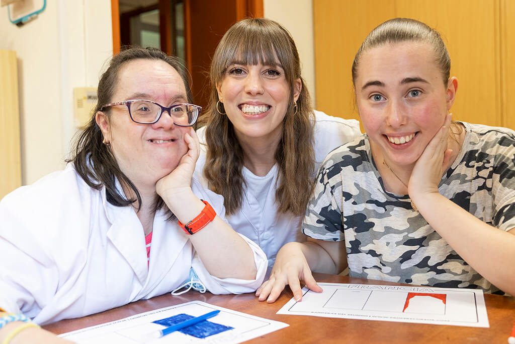 Foto de una trabajadora del centro sonriendo con dos chicas con discapacidad intelectual y del desarrollo